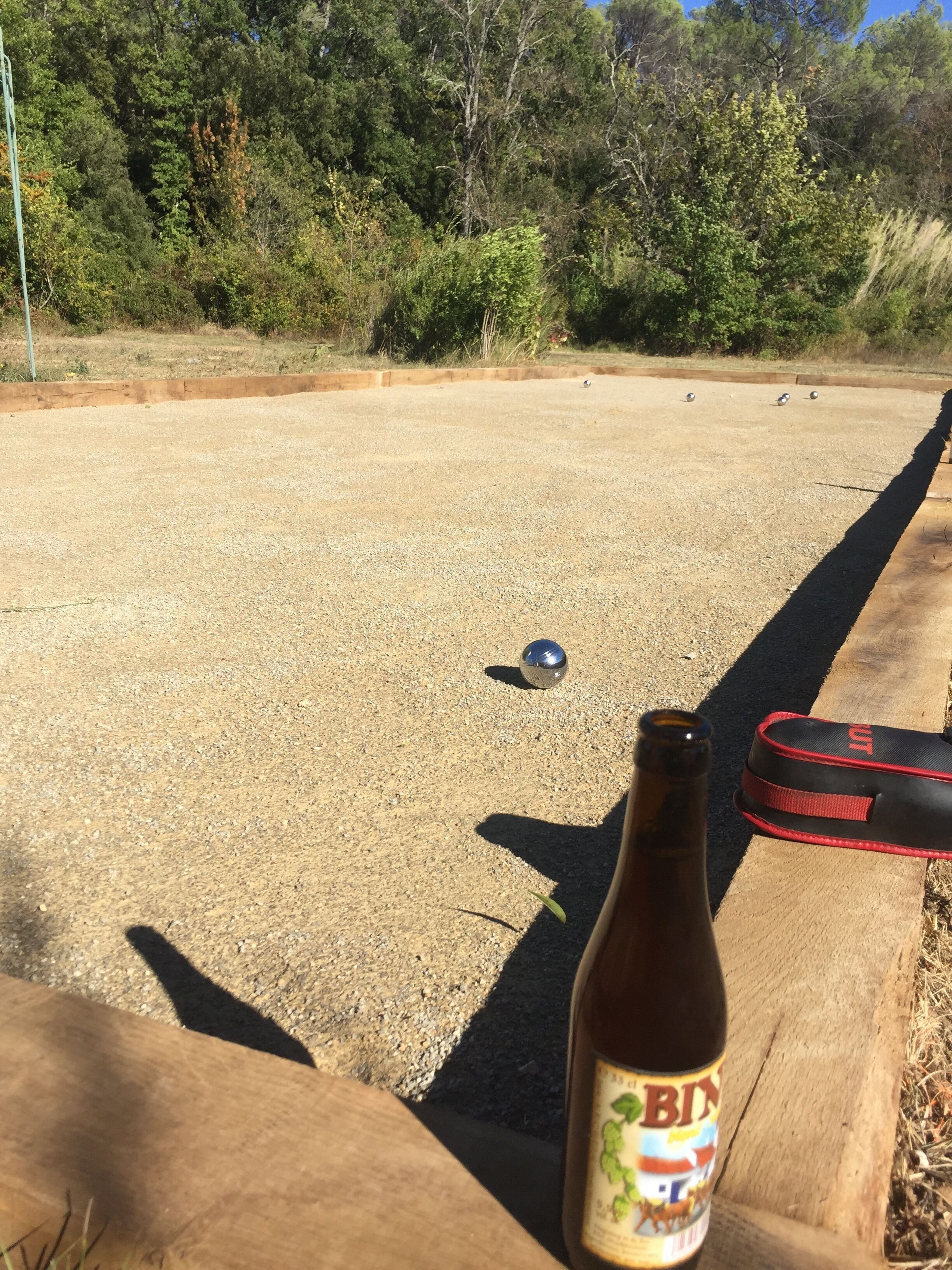 A bottle of beer on a wooden surface with a bowling alley in the background.