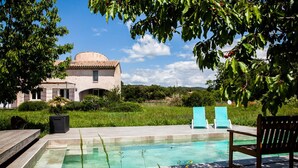A swimming pool with lounge chairs and a wooden bench, surrounded by greenery and a building with a dome roof. - Large villa, 6 to 15 people on the edge of the forest and river with heated pool (Cotignac)