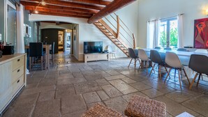 A spacious living area with a stone floor, wooden ceiling beams, a TV, and a dining area with chairs. - Large villa, 6 to 15 people on the edge of the forest and river with heated pool (Cotignac)