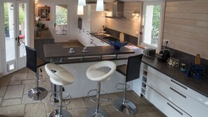 A modern kitchen with a central island, bar stools, and a view of the outdoors. - Large villa, 6 to 15 people on the edge of the forest and river with heated pool (Cotignac)