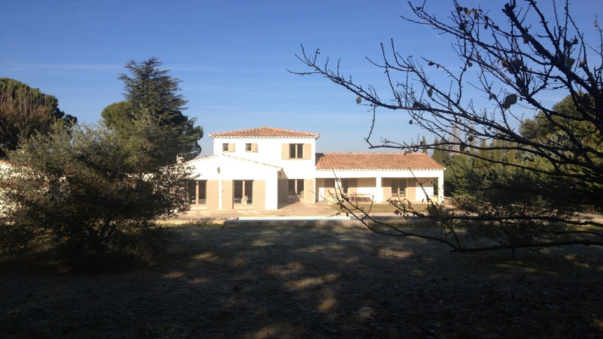 A two-story house with a tiled roof, surrounded by trees and a clear sky.
