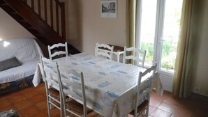 A dining area with a table set for four, surrounded by white chairs with woven seats. A staircase is visible in the background, leading to an upper level.