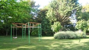 A swing set in a grassy area with trees and shrubs.