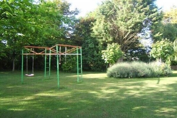 A swing set in a grassy area with trees and shrubs.
