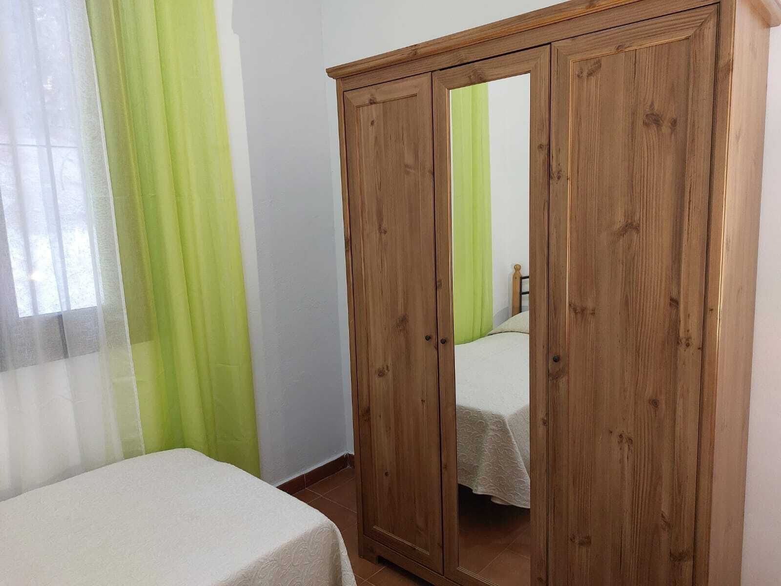 Ein Zimmer mit einem Bett, einem Kleiderschrank und einem Fenster mit leichtem Vorhang.