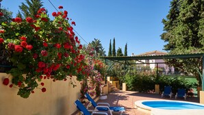 Ein Poolbereich mit Liegestühlen, einem Schwimmbecken und einer Wand, die mit roten Blumen geschmückt ist.