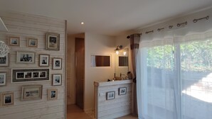 Une pièce avec un mur en bois orné de photographies encadrées, une commode blanche avec un miroir et une fenêtre avec des rideaux légers.