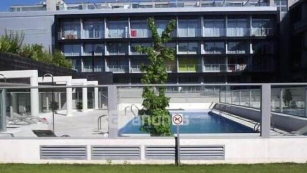 Un edificio moderno con piscina, un letrero que indica ‘no natación’ y un pequeño árbol en la fachada.