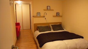 Un dormitorio con cama, una silla roja y un pasillo que conduce a una puerta.