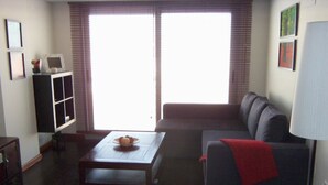 Una sala de estar con un sofá, una mesa de centro, un mueble para televisión y una ventana con persianas.