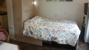 A small, single-bed room with a wooden wardrobe, a tiled floor, and a wall with framed artwork. - Studio with garden very close to the center of Thonon Baths (Thonon-Les-Bains)