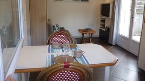 A dining area with a table set for two, a television, and a window with curtains. - Studio with garden very close to the center of Thonon Baths (Thonon-Les-Bains)