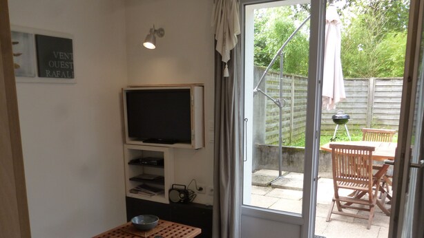A compact living space with a television, a small table with a bowl, and a sliding glass door leading to an outdoor patio with a table and chairs. - Studio with garden very close to the center of Thonon Baths (Thonon-Les-Bains)