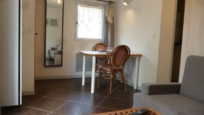 A dining area with a table and chairs, a mirror, a window with curtains, and a sofa. - Studio with garden very close to the center of Thonon Baths (Thonon-Les-Bains)