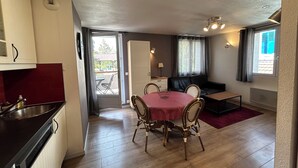 Ein kompakter Wohnraum mit Küchenzeile, einer Essecke mit Tisch und Stühlen, einer Couch und Blick durch eine Tür auf einen Außenbereich.