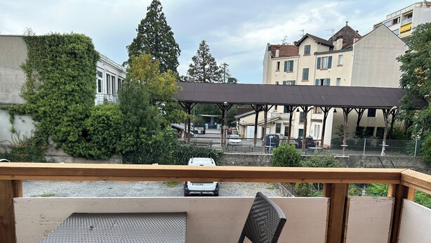 Eine Holzdiele mit Tisch und Stühlen, mit Blick auf eine Straße mit Gebäuden und einem überdachten Bereich.