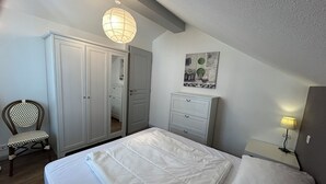 Ein Schlafzimmer mit Bett, Kleiderschrank, Sessel, Nachttisch mit Lampe und Wandbild.