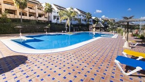 Une piscine avec une terrasse carrelée, des chaises longues et des palmiers.