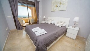Une chambre avec un grand lit, deux tables de chevet, une vue à travers une porte coulissante et un tableau au mur.