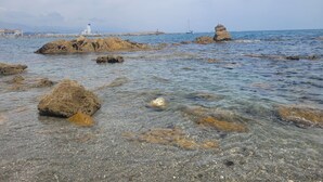 Un rivage rocheux bordé d’une eau claire, un phare et un voilier à l’horizon.