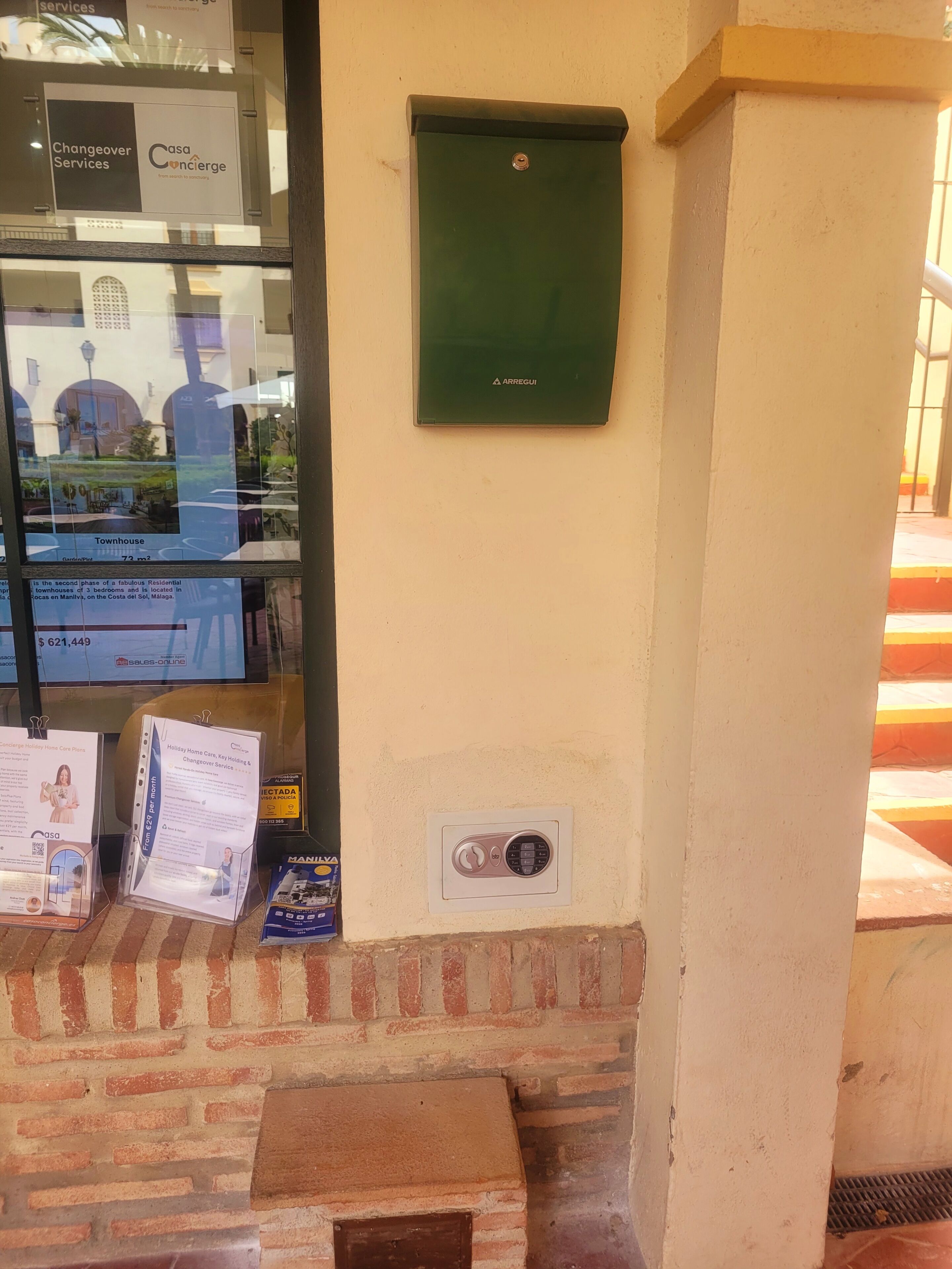 L’entrée d’un hôtel, avec une porte en verre, un panneau de service vert et des brochures d’information affichées sur le mur.