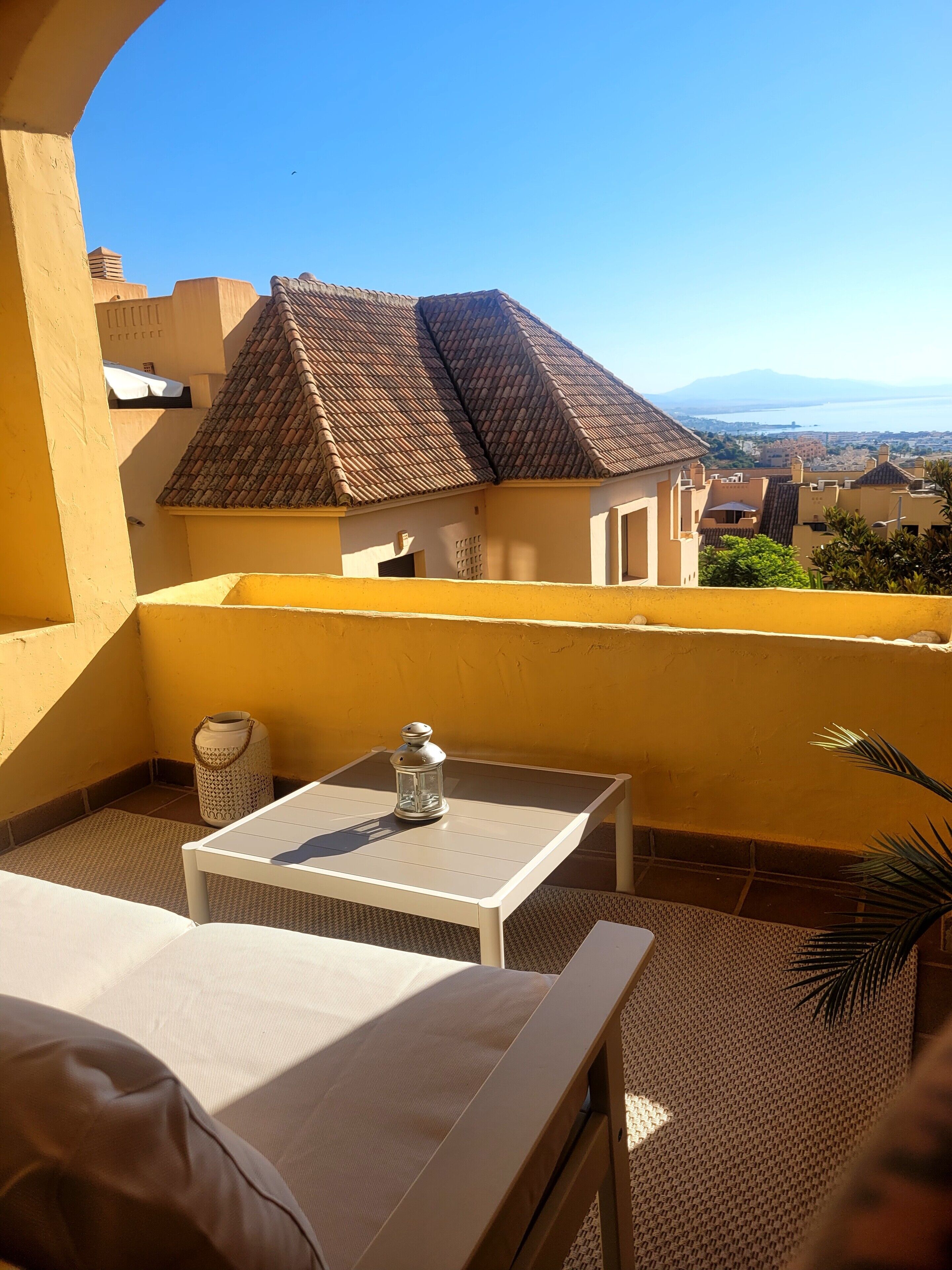 Varanda com mesa e cadeiras, um candeeiro e vista para prédios e paisagem distante.