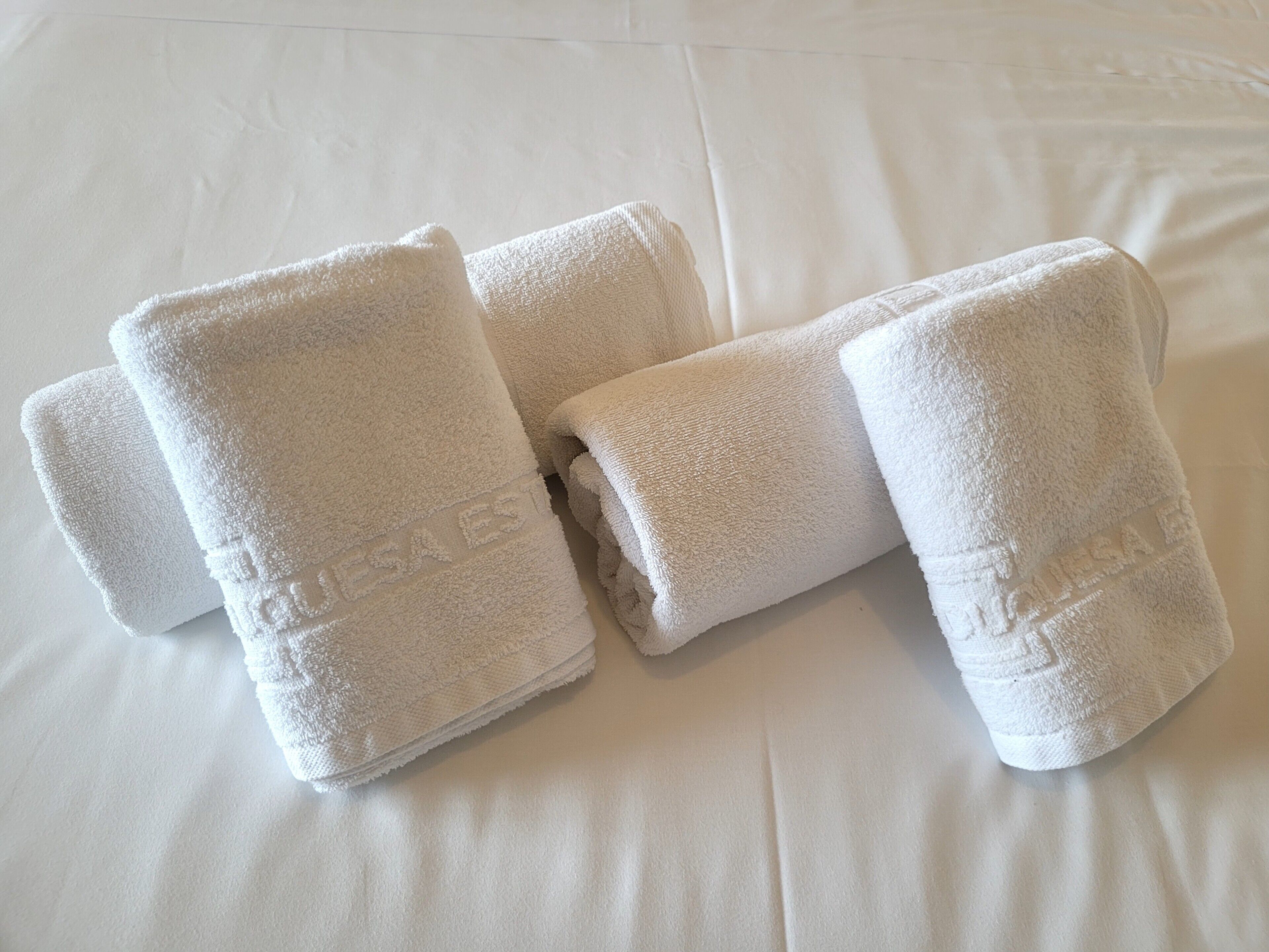 Four neatly folded white towels on a bed with a smooth, white surface.