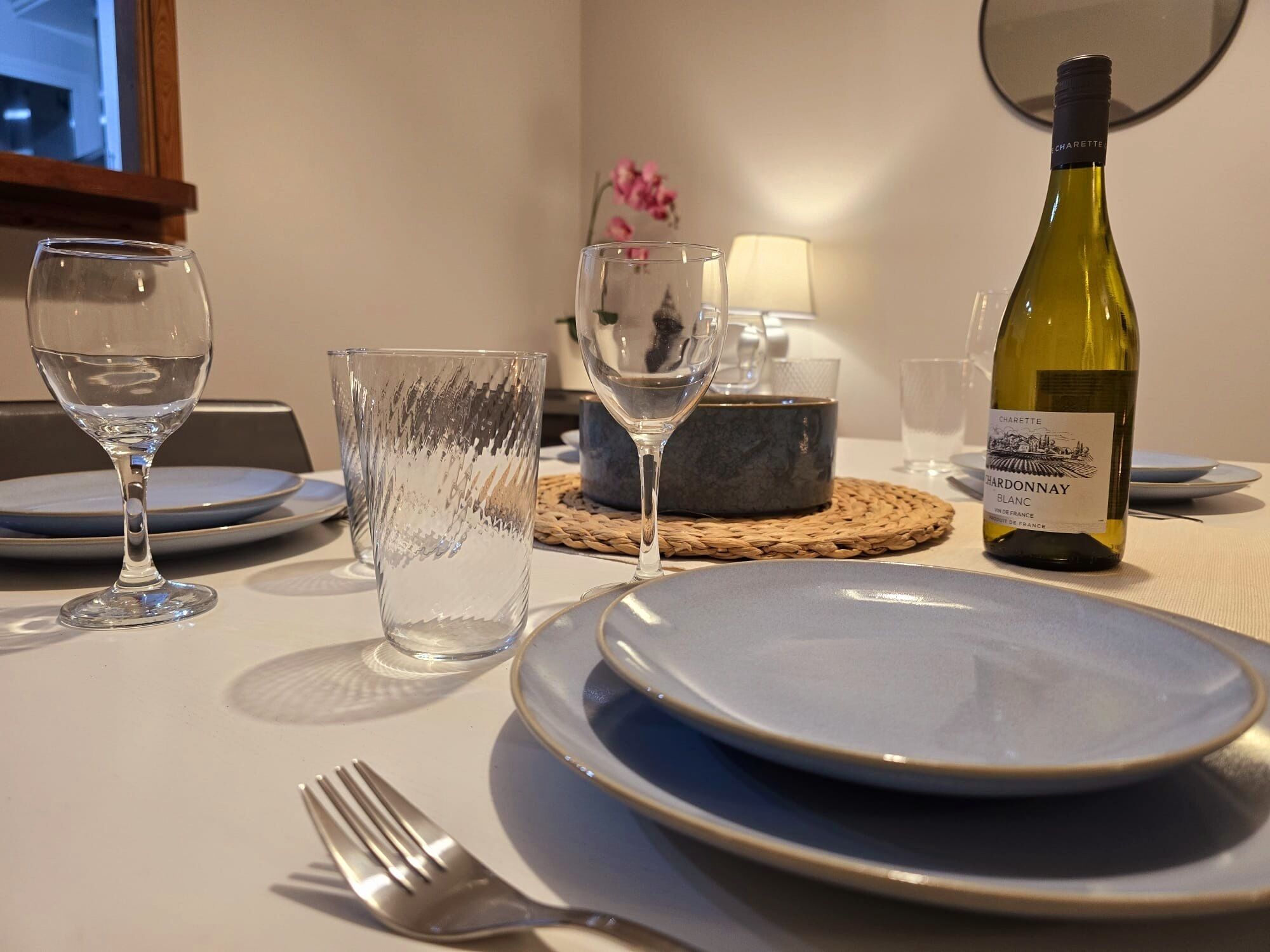 Een eettafel gedekt met borden, glazen, een wijnfles en een vork.