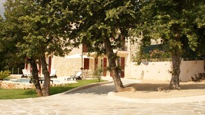 A stone pathway leading to a building with a pool, surrounded by trees and outdoor seating.