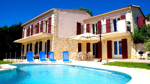 A two-story building with a swimming pool, outdoor seating, and a stone facade.