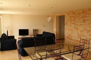 A living room with a glass table, black sofas, a TV, and a bookshelf.
