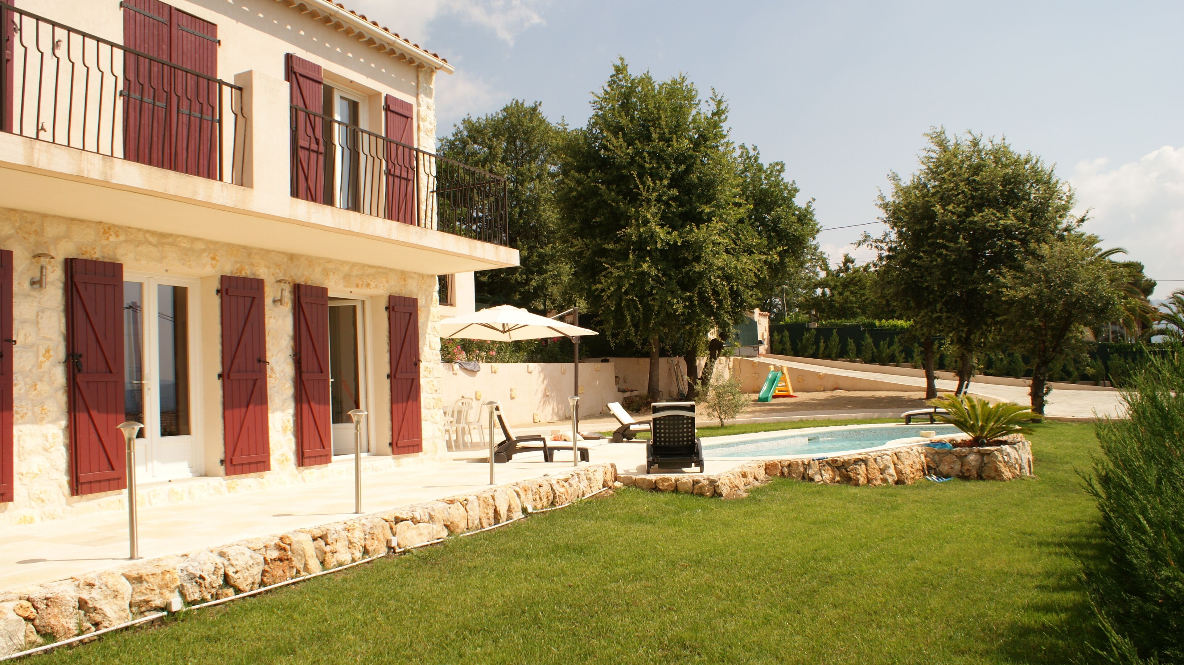 A two-story house with a swimming pool, outdoor seating, and a stone wall.