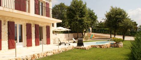 A two-story house with a swimming pool, outdoor seating, and a stone wall.