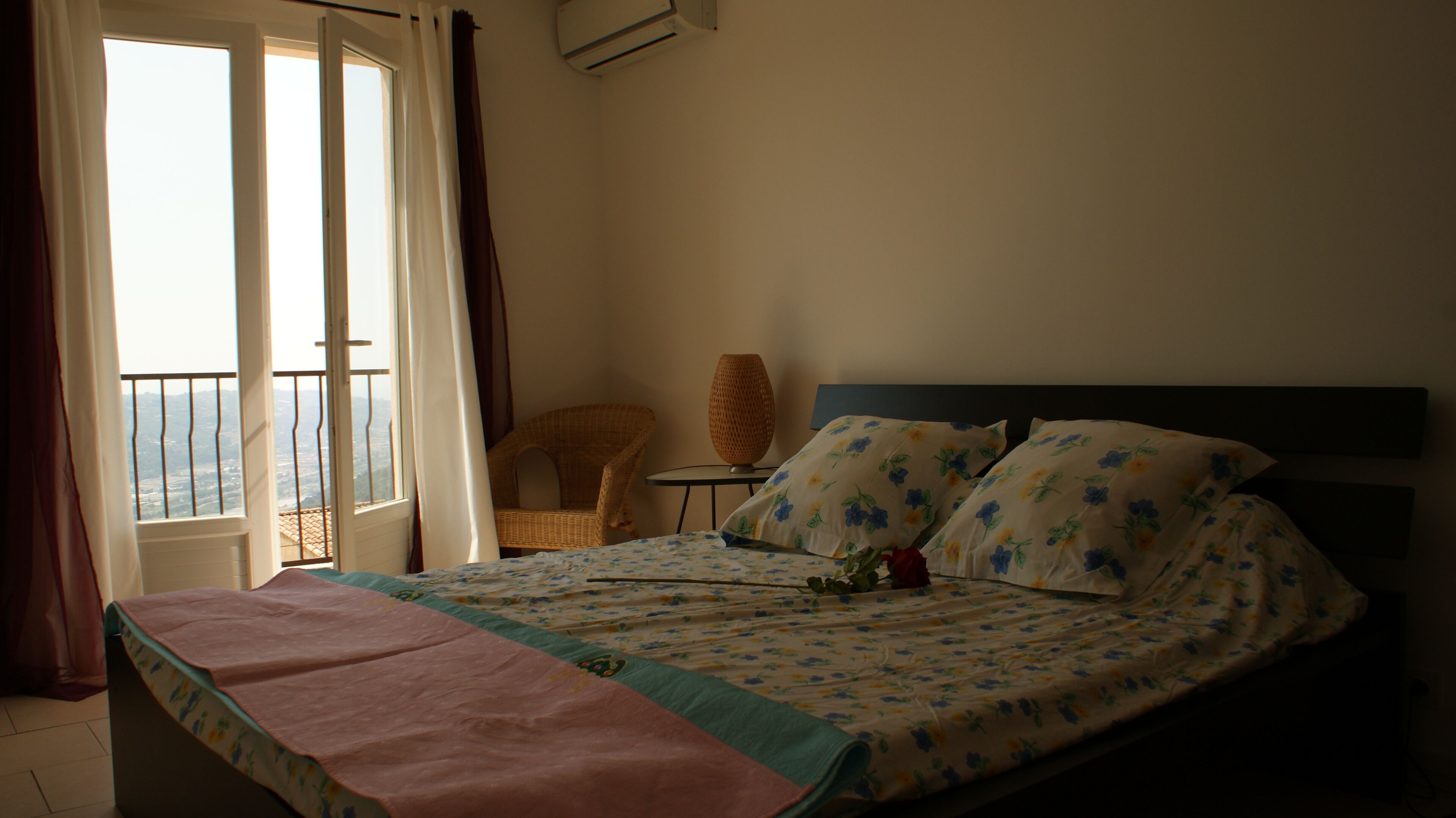 A bedroom with a bed, a chair, a small table, and a view of the outside.