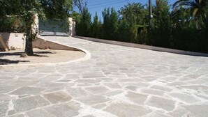 A paved courtyard with stone tiles, surrounded by trees and a low wall.