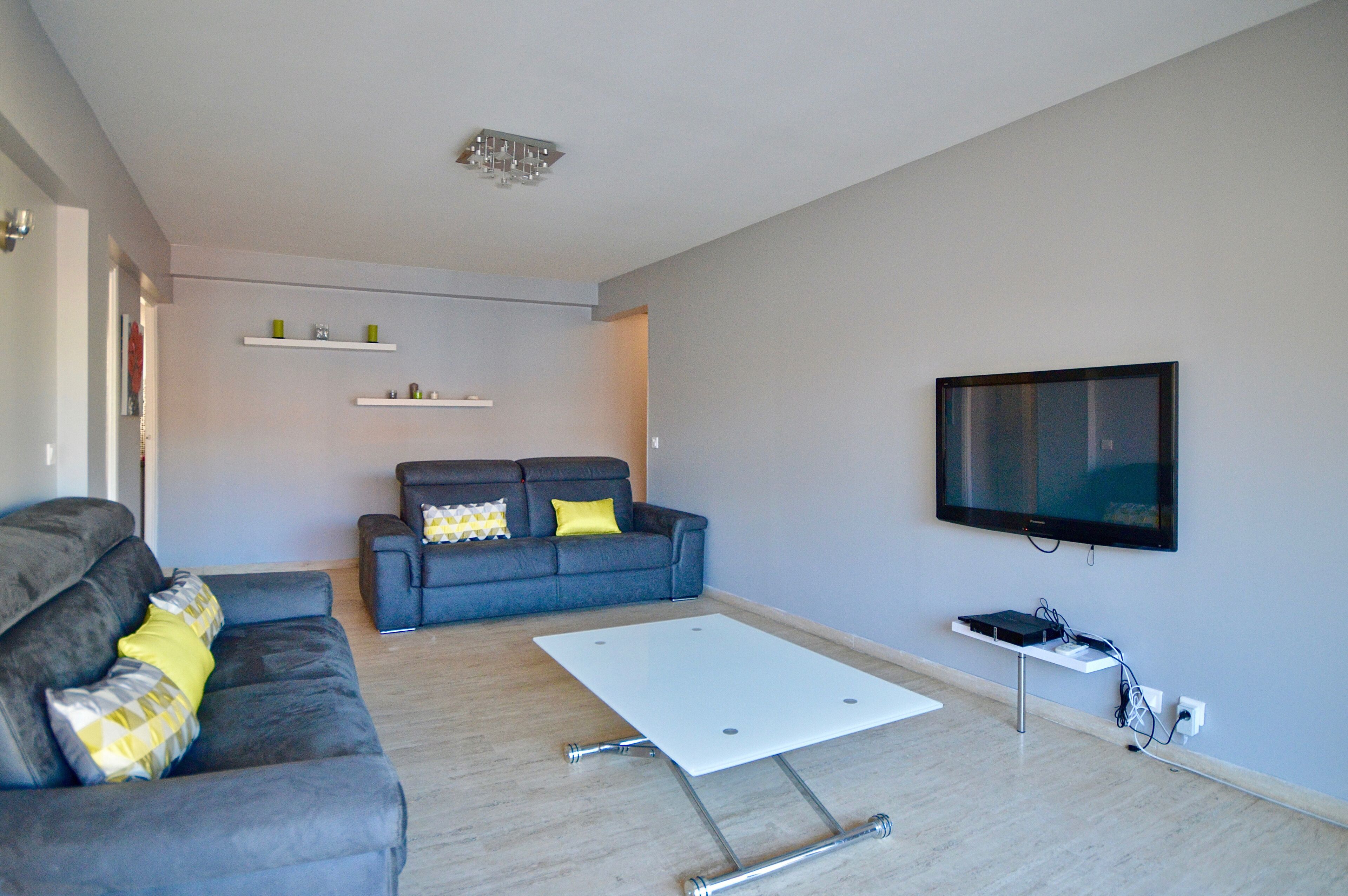 A modern living room with a grey sofa, a white coffee table, and a flat-screen TV mounted on the wall.