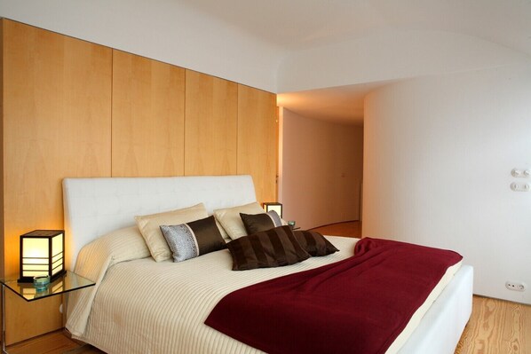 A modern bedroom with a large bed, a wooden headboard, and a bedside table with a lamp.