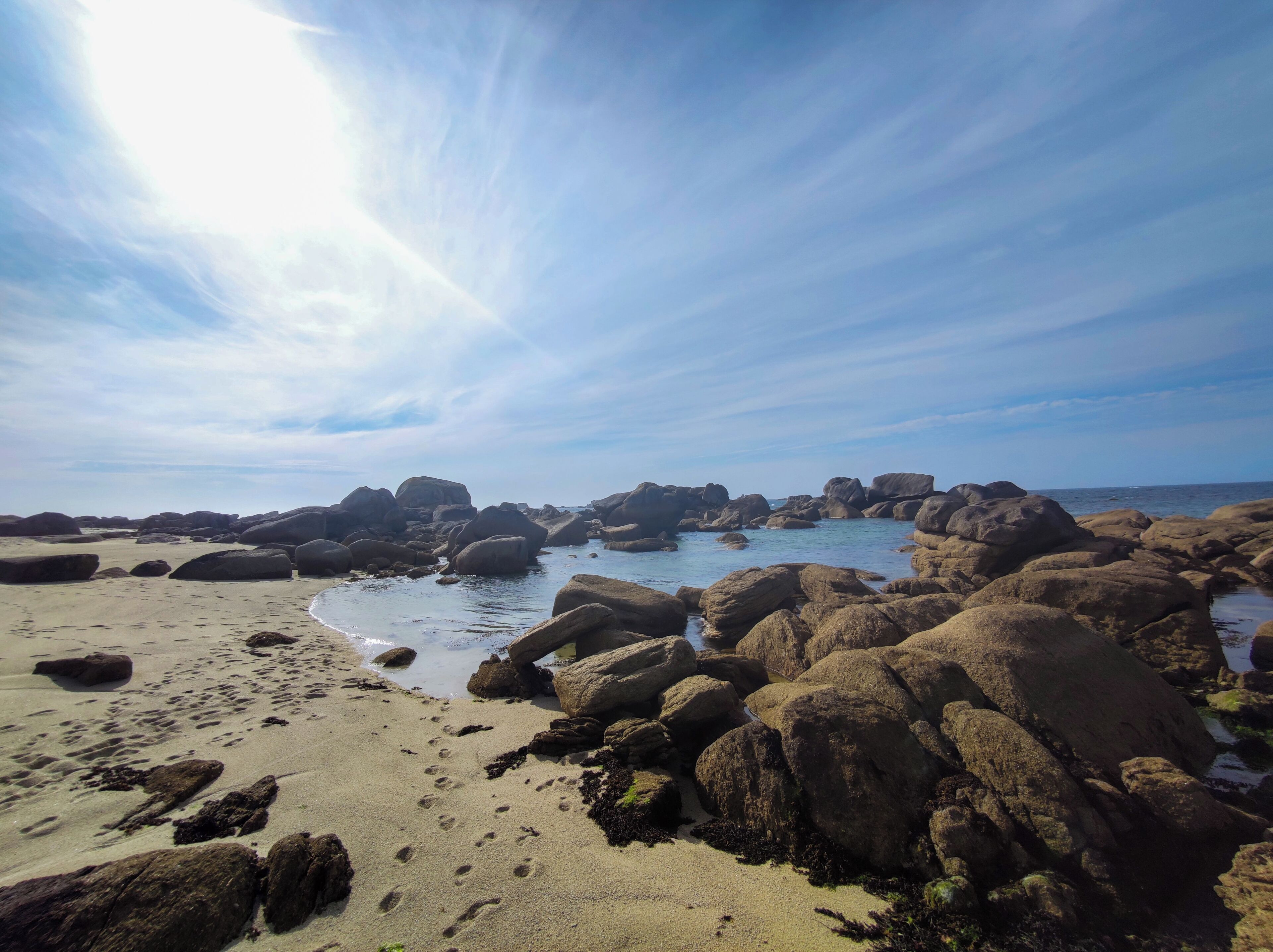 Uma praia rochosa com grandes pedregulhos e céu claro.
