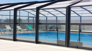 A pool area with clear glass walls, lounge chairs, and a blue pool.