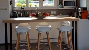 A kitchen with a central island, three bar stools, a microwave, and a refrigerator.