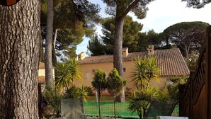 A garden with two black lounge chairs, a small tree, and a building with a tiled roof in the background. - Studio Seaside - Saint Cyr sur Mer (Les Lecques) (Saint-Cyr-sur-Mer)