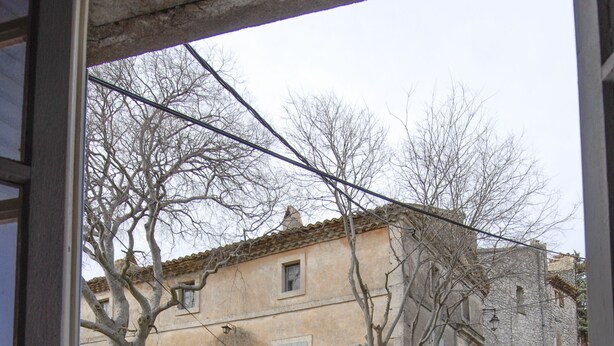 Blick auf ein Steingebäude mit einem Fenster, einem Baum und einer Steinmauer.