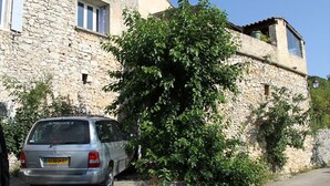 Ein Steingebäude mit einem geparkten Auto und einem großen Baum davor.