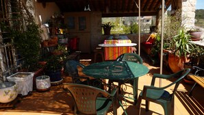 Eine Terrasse mit Tisch und Stühlen, umgeben von Blumentöpfen und einem rustikalen Gebäude.