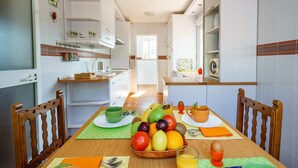 A modern kitchen with white cabinets, a dining table set with fruits and drinks, and a view into the adjacent living area.