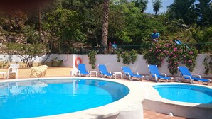 A pool area with two separate pools, lounge chairs, and a person standing on a platform.