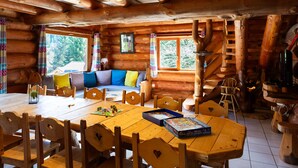 A log cabin interior with a wooden dining table, chairs, a sofa, and a staircase. - Superbe chalet rondins de 150 m² au cœur des Vosges, sauna, wifi, groupe, famille (La Bresse)