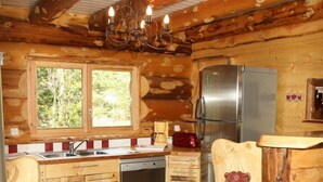 A log cabin kitchen with a dishwasher, refrigerator, and a window with a view of trees. - Superbe chalet rondins de 150 m² au cœur des Vosges, sauna, wifi, groupe, famille (La Bresse)