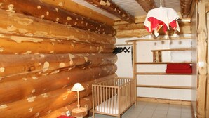 A log cabin interior with a crib, a hanging light, and a shelf with a red pillow. - Superbe chalet rondins de 150 m² au cœur des Vosges, sauna, wifi, groupe, famille (La Bresse)