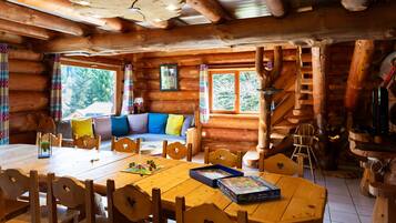 Cozy cabin with a large dining table, comfortable sofa, and a spiral staircase leading to additional sleeping quarters.